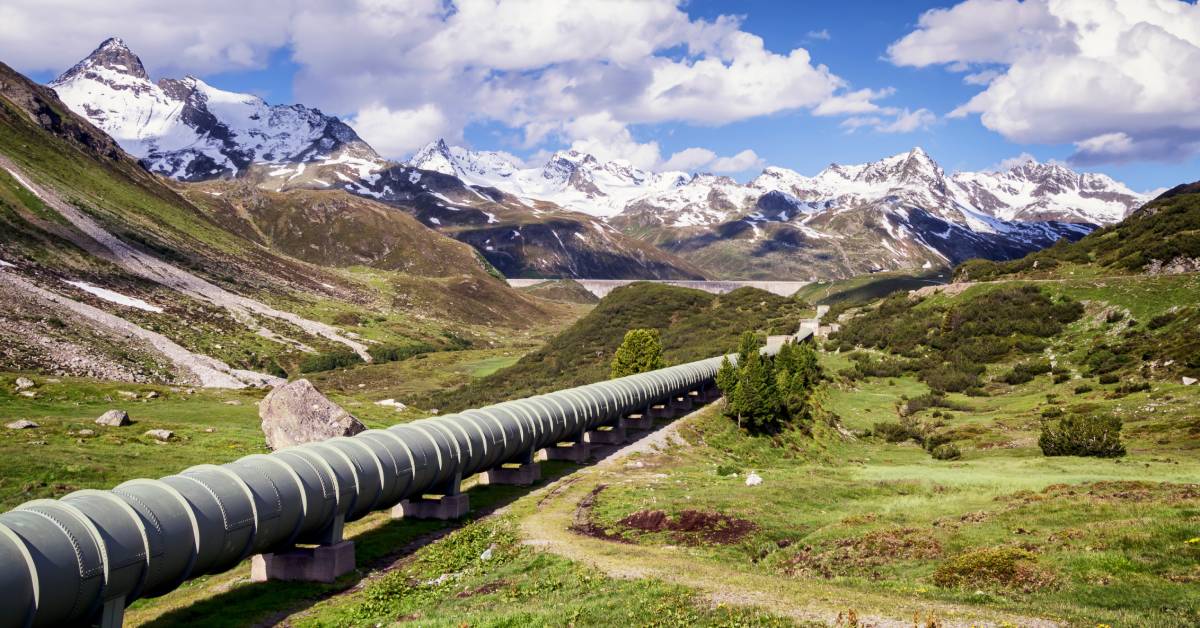 A very large, long pipeline winding through a beautiful valley surrounded by snow-capped mountains.